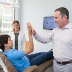 Dr Michael Stewart with young male patient , giving him a high five and assistant in his dental office at Stewart & Arango Oral Surgery